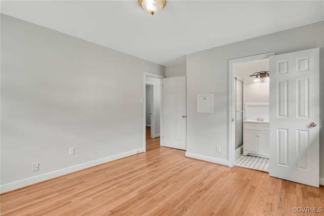 unfurnished bedroom with light wood-type flooring, baseboards, and ensuite bath