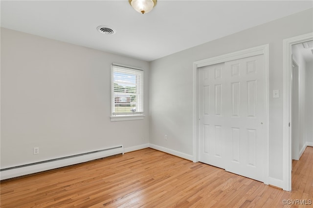 unfurnished bedroom with a baseboard radiator, light wood finished floors, baseboards, and a closet