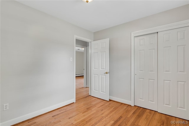 unfurnished bedroom with baseboards, light wood finished floors, a closet, and a baseboard radiator