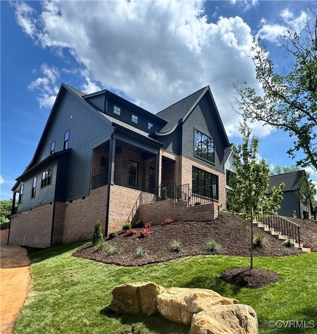view of side of home featuring brick siding, stairway, covered porch, and a yard
