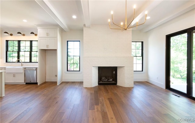 unfurnished living room featuring beamed ceiling, a sink, light wood-style flooring, baseboards, and a chandelier