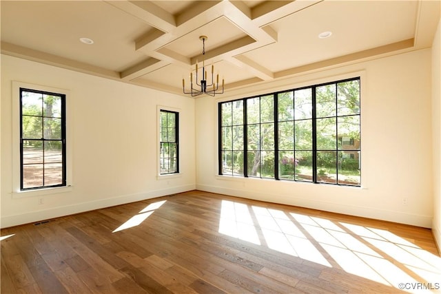 empty room with coffered ceiling, healthy amount of natural light, baseboards, a chandelier, and wood-type flooring