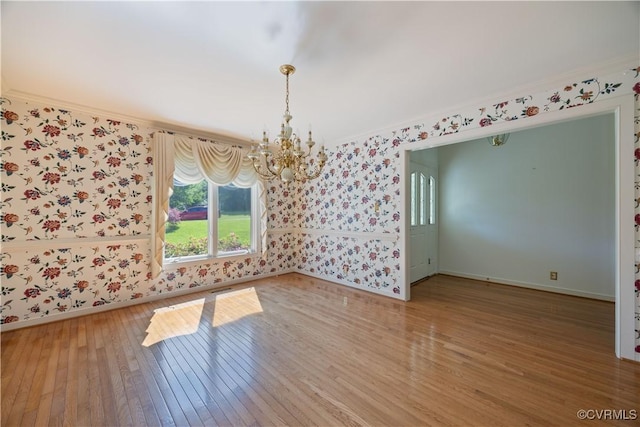 unfurnished dining area featuring wallpapered walls, a chandelier, baseboards, hardwood / wood-style flooring, and ornamental molding