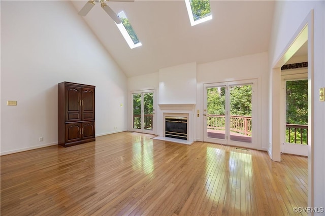 unfurnished living room with high vaulted ceiling, a skylight, light wood-type flooring, ceiling fan, and a glass covered fireplace