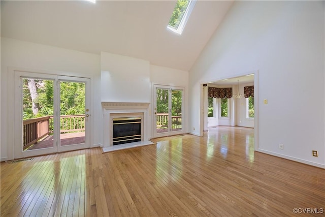unfurnished living room with high vaulted ceiling, hardwood / wood-style flooring, a glass covered fireplace, and baseboards