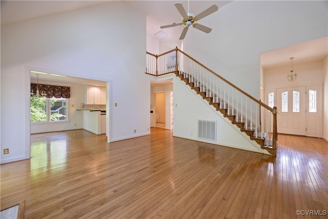 unfurnished living room featuring a towering ceiling, stairway, light wood-type flooring, a chandelier, and a ceiling fan