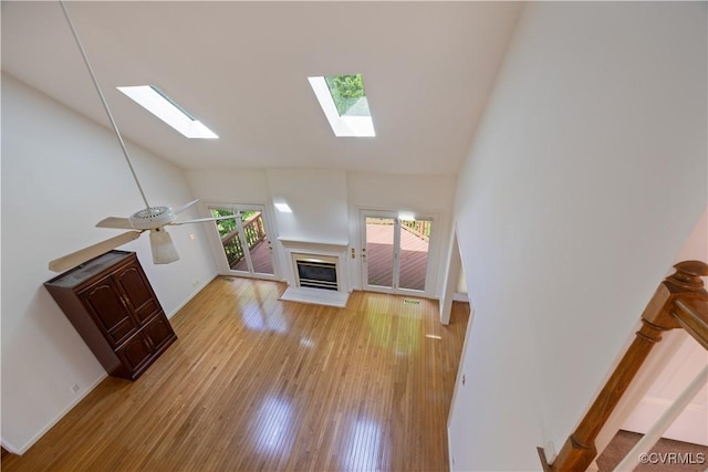 unfurnished living room with a skylight, high vaulted ceiling, a glass covered fireplace, light wood-style flooring, and baseboards
