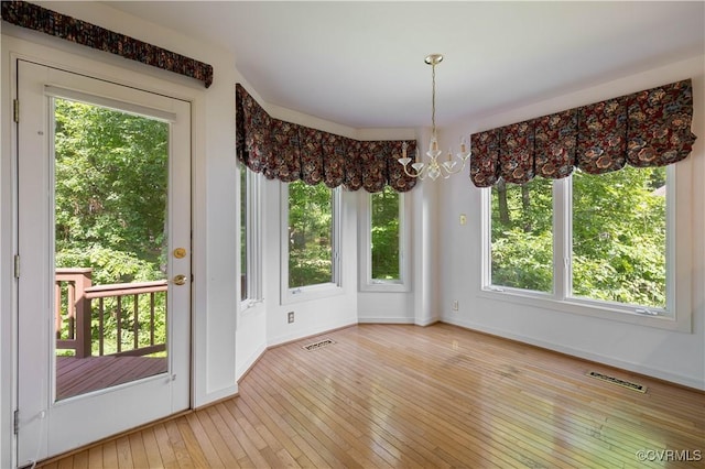 unfurnished dining area with a chandelier, hardwood / wood-style floors, and plenty of natural light