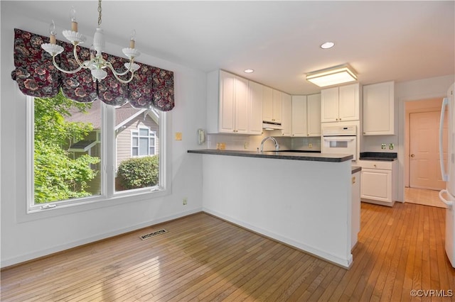 kitchen featuring white appliances, under cabinet range hood, white cabinets, light wood finished floors, and dark countertops