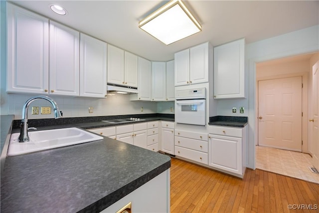 kitchen featuring oven, a sink, under cabinet range hood, electric cooktop, and white cabinets