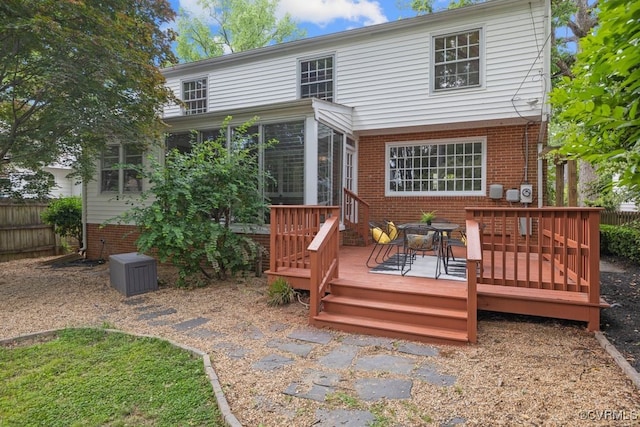 rear view of property with a sunroom, brick siding, a wooden deck, and fence