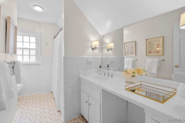 full bath with toilet, tile walls, vanity, a wainscoted wall, and lofted ceiling