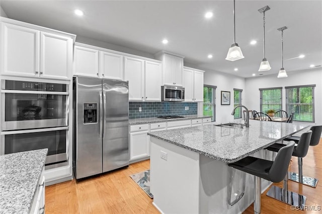 kitchen featuring appliances with stainless steel finishes, a sink, white cabinetry, light wood-style floors, and recessed lighting