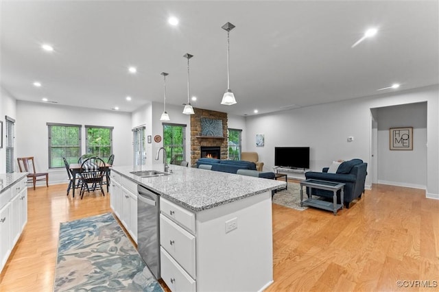 kitchen with a sink, white cabinetry, dishwasher, a stone fireplace, and recessed lighting