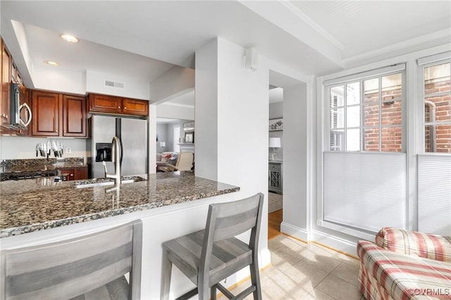 kitchen featuring appliances with stainless steel finishes, dark stone countertops, a breakfast bar area, a sink, and a peninsula