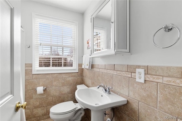 half bathroom featuring toilet, a sink, wainscoting, and tile walls