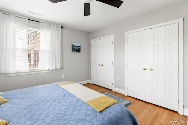bedroom with multiple closets, wood finished floors, a ceiling fan, and baseboards