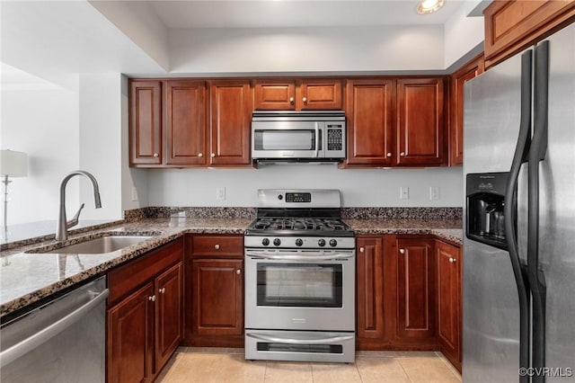 kitchen featuring stainless steel appliances, a sink, dark stone counters, and light tile patterned floors