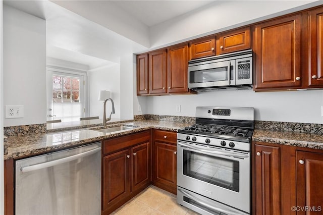kitchen with stainless steel appliances, a sink, dark stone counters, light tile patterned flooring, and brown cabinets