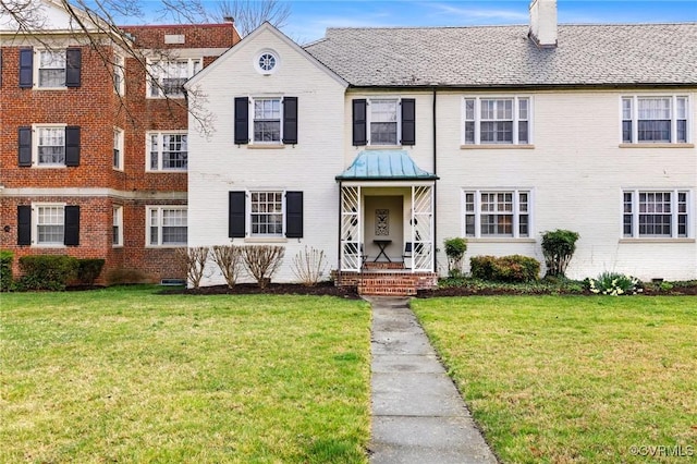 view of property featuring a chimney, a front lawn, and brick siding