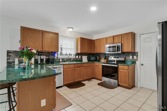 kitchen with stainless steel appliances, a peninsula, decorative backsplash, brown cabinetry, and a kitchen bar