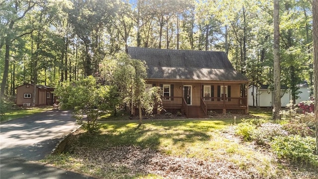 cape cod home with covered porch, driveway, a shingled roof, and an outdoor structure