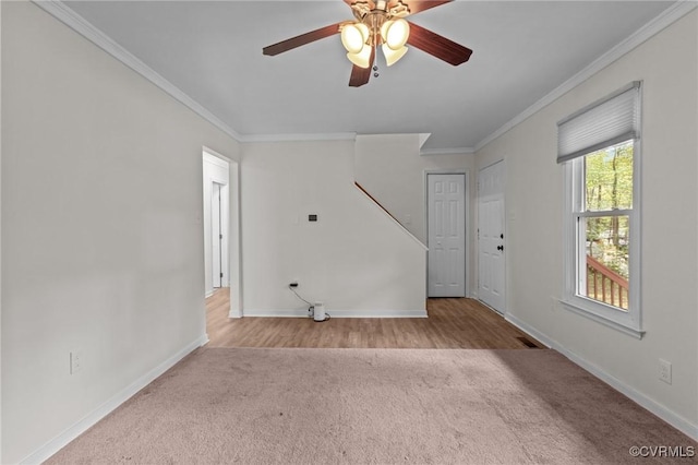 unfurnished living room featuring carpet, crown molding, baseboards, ceiling fan, and stairway