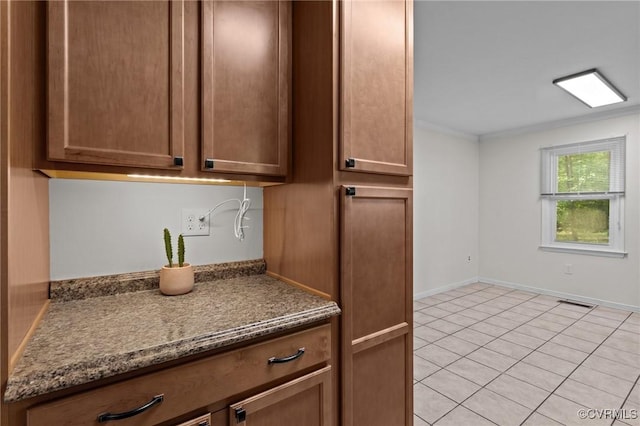 kitchen featuring light tile patterned floors, ornamental molding, dark stone countertops, and baseboards