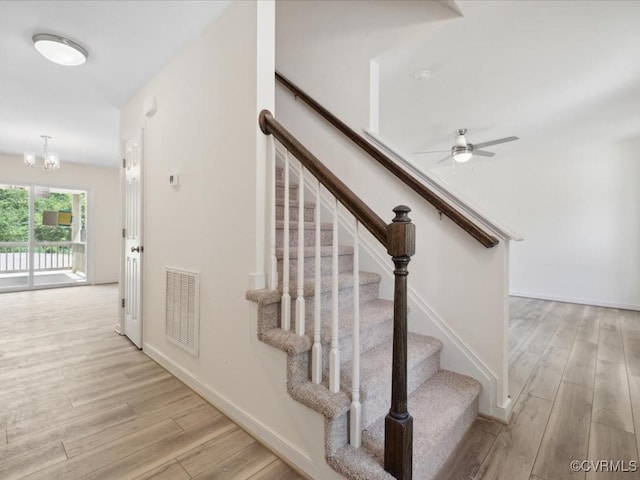stairway featuring wood finished floors, a ceiling fan, a chandelier, and baseboards