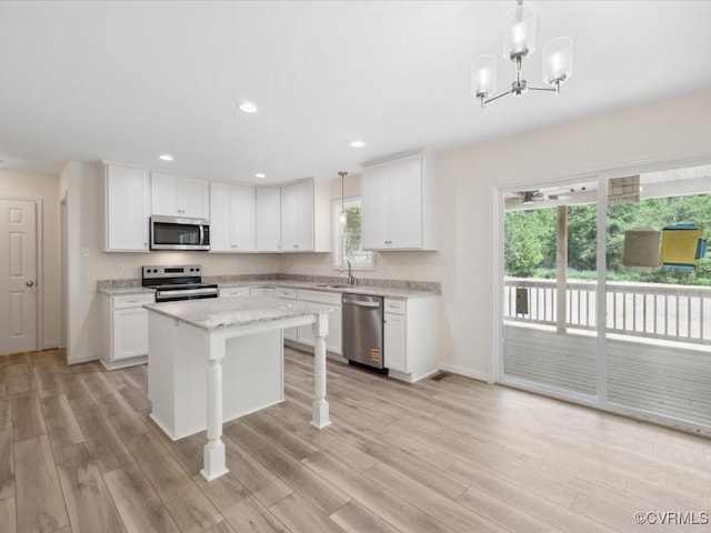 kitchen with appliances with stainless steel finishes, a kitchen island, a sink, white cabinets, and light wood-style flooring