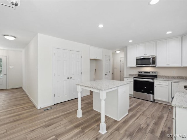 kitchen with stainless steel appliances, light wood-style floors, white cabinets, light stone countertops, and recessed lighting