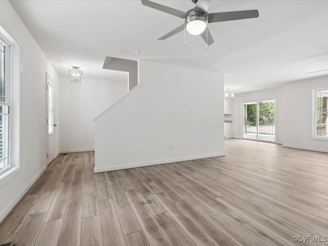 unfurnished living room with a chandelier, light wood-style floors, a ceiling fan, and baseboards