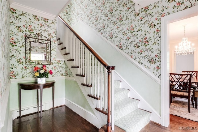 stairway with wallpapered walls, wood finished floors, ornamental molding, a chandelier, and a wainscoted wall