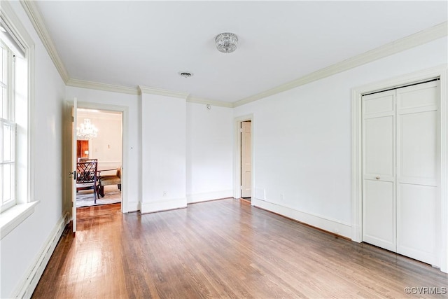 unfurnished bedroom with baseboard heating, wood finished floors, a chandelier, ornamental molding, and baseboards