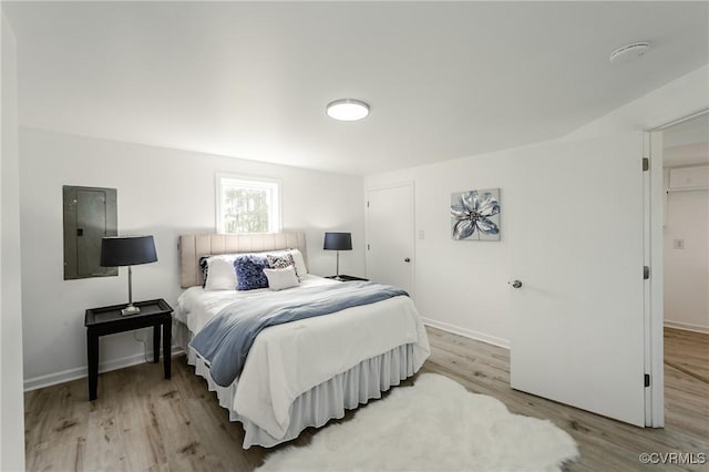 bedroom with electric panel, light wood-type flooring, and baseboards