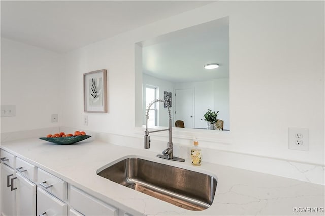 kitchen with a sink, white cabinets, and light stone counters