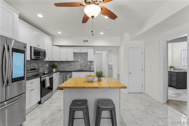 1216 N 30th St, Richmond, VA 23223 - kitchen with stainless steel appliances, wood counters, a breakfast bar area, decorative backsplash, and white cabinetry