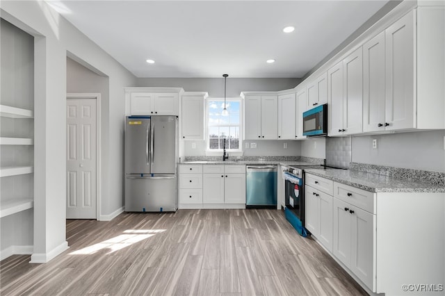 kitchen featuring stainless steel appliances, white cabinetry, light wood finished floors, baseboards, and light stone countertops