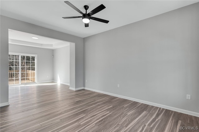 empty room featuring wood finished floors, baseboards, and a ceiling fan