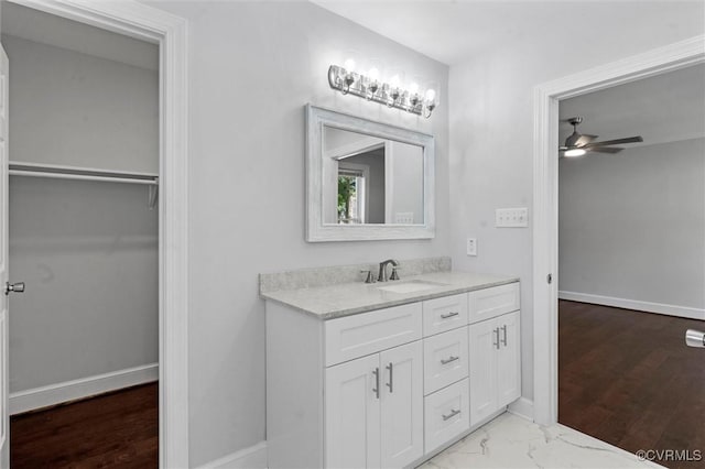 bathroom featuring vanity, a ceiling fan, baseboards, a walk in closet, and wood finished floors