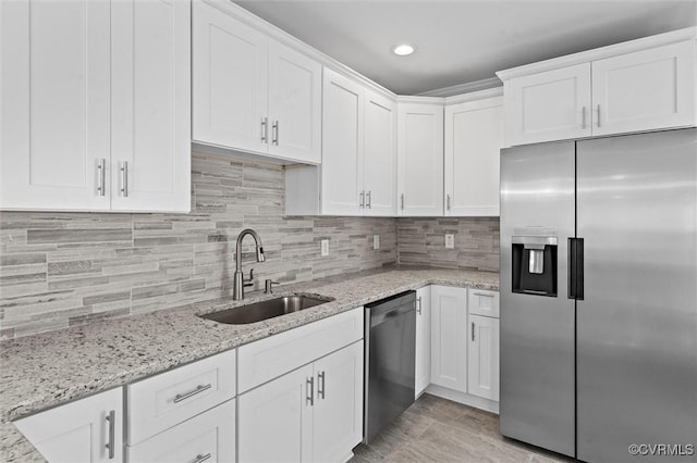 kitchen with appliances with stainless steel finishes, a sink, white cabinets, decorative backsplash, and light stone counters