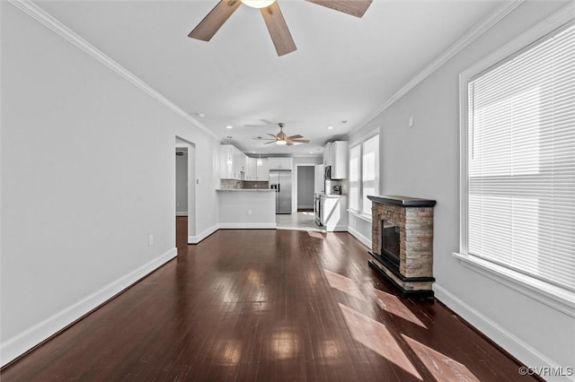 unfurnished living room featuring ceiling fan, ornamental molding, dark wood-style floors, baseboards, and a stone fireplace