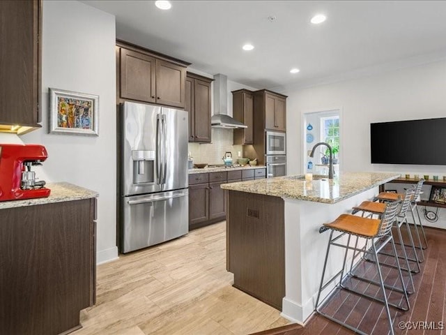 5435 Libbie Mill W Blvd, Henrico, VA 23230 - kitchen with stainless steel appliances, wall chimney exhaust hood, a sink, light wood-style flooring, and a kitchen bar