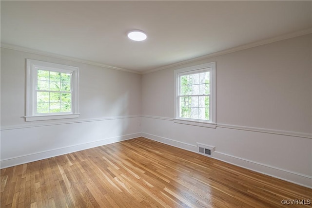 empty room featuring crown molding, plenty of natural light, light wood-style flooring, and baseboards