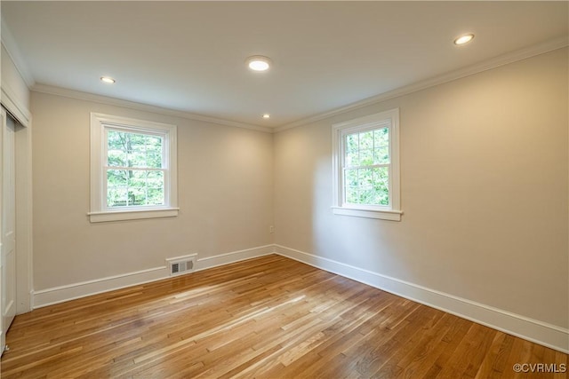 spare room featuring healthy amount of natural light, light wood finished floors, baseboards, ornamental molding, and recessed lighting