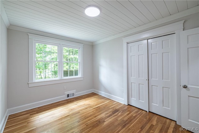 unfurnished bedroom with crown molding, wood finished floors, baseboards, wood ceiling, and a closet