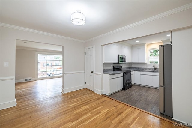 kitchen with appliances with stainless steel finishes, light wood-type flooring, a sink, white cabinets, and crown molding