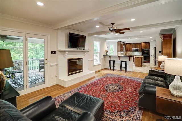 living area with ornamental molding, ceiling fan, light wood-type flooring, a brick fireplace, and recessed lighting