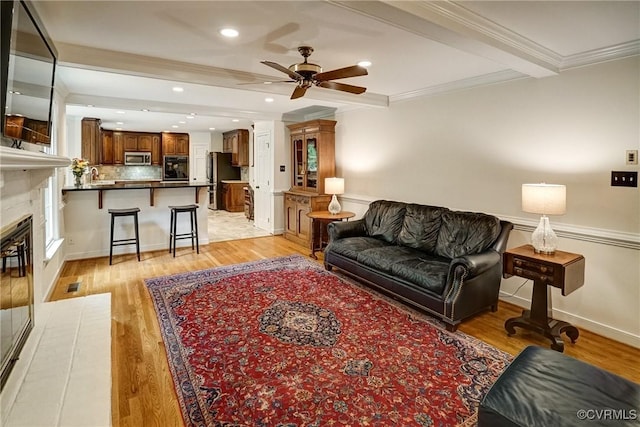 living room with a ceiling fan, crown molding, light wood-style floors, recessed lighting, and a glass covered fireplace