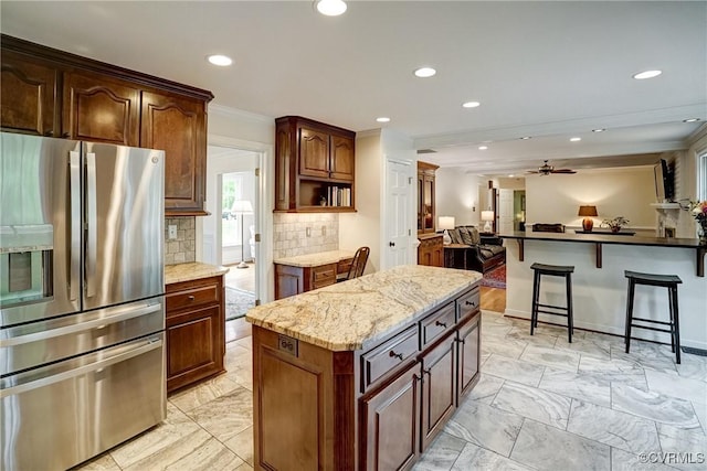 kitchen with stainless steel refrigerator with ice dispenser, open floor plan, recessed lighting, tasteful backsplash, and a breakfast bar